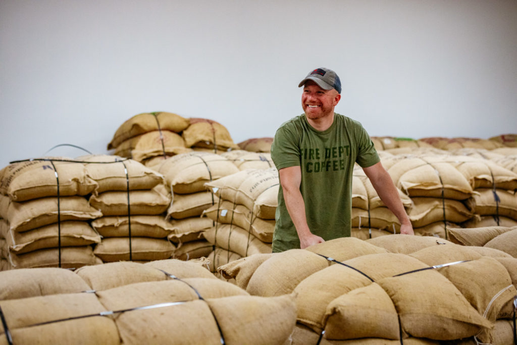 Fire Dept Coffee founder and CEO Luke Schneider standing with bags of coffee beans.